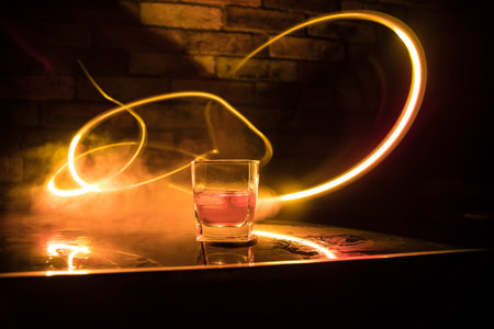 Whiskey drink concept. Glass of whiskey and ice with color light and fog on dark bar background. selective focusの写真素材