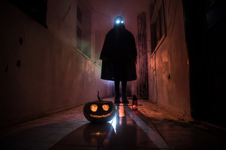 Halloween concept. Creepy silhouette in the dark corridor with pumpkin head. Toned light with fog on background. selective focus. long shutter shotの写真素材