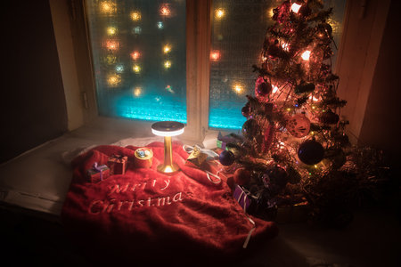 Christmas and New year concept.Fir tree standing on red carpet with traditional holiday attributes. Cozy window with colorful lights on background. selective focusの写真素材