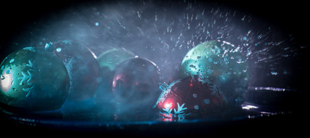 New year and Christmas concept. Glass bauble dropped into water or water splash on dark foggy background. selective focus.の写真素材