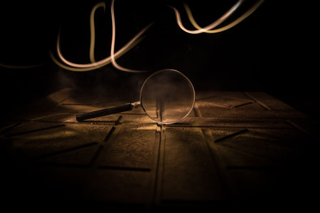 Magnifying glass on stone surface in dark background, under the light, mysterious detective conceptの写真素材