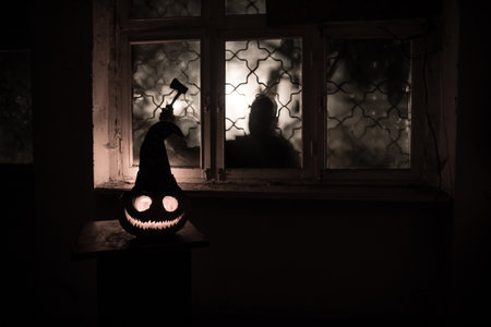 Scary Halloween pumpkin in the mystical house window at night or halloween pumpkin and horror silhouette in window. selective focusの写真素材