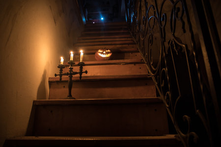 Horror Halloween concept. Creepy abandoned castle. An old candlestick and Halloween pumpkin glowing on wooden stairs with lattice door at night. Decoration with backlight and fog. selective focusの写真素材