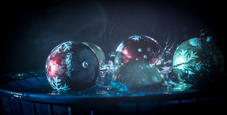 New year and Christmas concept. Glass bauble dropped into water or water splash on dark foggy background. selective focus.の写真素材