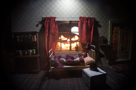 Horror Halloween concept. A realistic dollhouse bedroom with furniture and window at night. Scared man in bed with giant glowing pumpkin. selective focusの写真素材