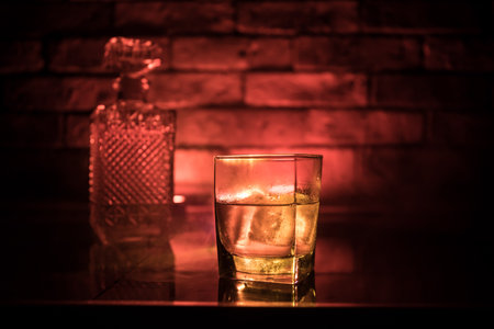 Whiskey drink concept. Glass of whiskey and ice with color light and fog on dark bar background. selective focusの写真素材