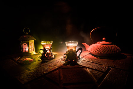 Arabian tea in glass with eastern snacks on a stone surface on dark background with lights and smoke. Eastern tea concept. selective focus.の写真素材