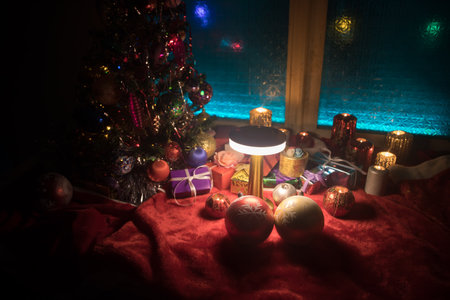 Christmas and New year concept.Fir tree standing on red carpet with traditional holiday attributes. Cozy window with colorful lights on background. selective focusの写真素材
