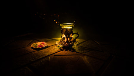 Arabian tea in glass with eastern snacks on a stone surface on dark background with lights and smoke. Eastern tea concept. selective focus.の写真素材