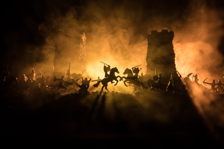 Medieval battle scene with cavalry and infantry. Silhouettes of figures as separate objects, fight between warriors on dark toned foggy background. Night scene. Selective focusの写真素材