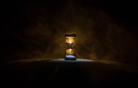 Hourglass as time passing concept for business deadline, urgency and running out of time. Sandglass, egg timer on dark background showing the last second or last minute or time out. With copy space.の写真素材