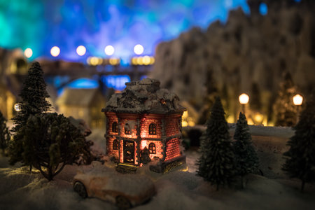 Little decorative cute small houses in snow at night in winter, Christmas and New Year miniature house in the snow at night with fir tree. Holiday concept. Selective focusの写真素材