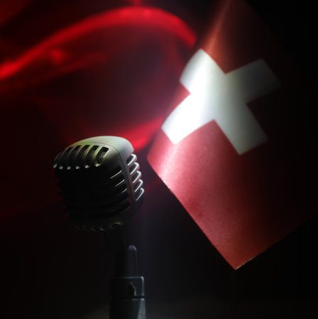 Microphone on a background of a blurry flag of Switzerland close-up. dark table decoration. Selective focusの写真素材