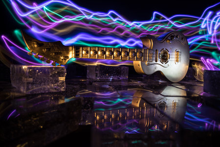 Music Concept: Guitar Miniature on a Dark Background with Vivid Light, Smoke, and Fire Effects. Golden electro guitar under a Dramatic Spotlight. Ice Glass blocks decorの写真素材