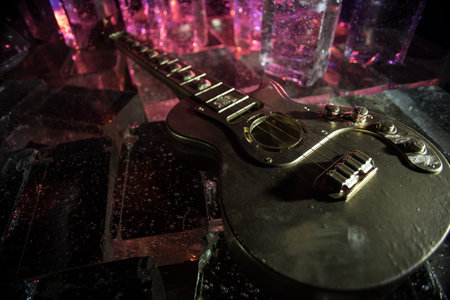 Music Concept: Guitar Miniature on a Dark Background with Vivid Light, Smoke, and Fire Effects. Golden electro guitar under a Dramatic Spotlight. Ice Glass blocks decorの写真素材