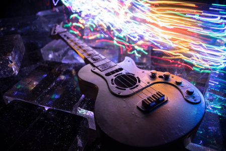 Music Concept: Guitar Miniature on a Dark Background with Vivid Light, Smoke, and Fire Effects. Golden electro guitar under a Dramatic Spotlight. Ice Glass blocks decorの写真素材