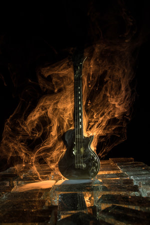 Music Concept: Guitar Miniature on a Dark Background with Vivid Light, Smoke, and Fire Effects. Golden electro guitar under a Dramatic Spotlight. Ice Glass blocks decorの写真素材