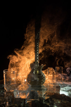 Music Concept: Guitar Miniature on a Dark Background with Vivid Light, Smoke, and Fire Effects. Golden electro guitar under a Dramatic Spotlight. Ice Glass blocks decorの写真素材
