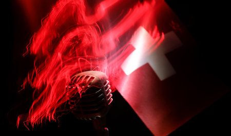 Microphone on a background of a blurry flag of Switzerland close-up. dark table decoration. Selective focusの写真素材