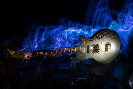 Music Concept: Guitar Miniature on a Dark Background with Vivid Light, Smoke, and Fire Effects. Golden electro guitar under a Dramatic Spotlight. Ice Glass blocks decorの写真素材