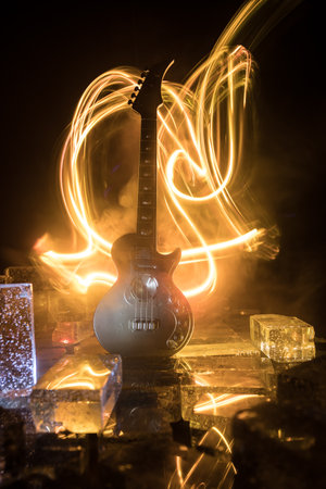 Music Concept: Guitar Miniature on a Dark Background with Vivid Light, Smoke, and Fire Effects. Golden electro guitar under a Dramatic Spotlight. Ice Glass blocks decorの写真素材