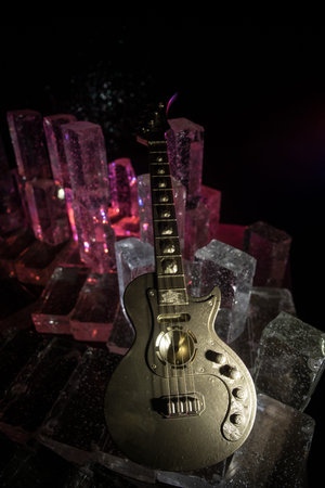 Music Concept: Guitar Miniature on a Dark Background with Vivid Light, Smoke, and Fire Effects. Golden guitar under a Dramatic Spotlight. Ice Glass blocks decorの写真素材