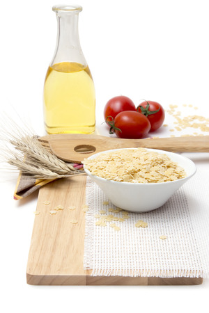 Italian pasta, macaroni  stelline for soup with cherry tomatoes and olive oil in a glass bottle on a wooden board, white backgroundの写真素材
