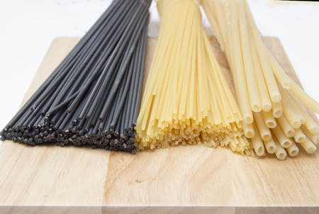 black and golden spaghetti, pasta of various kinds, on a wooden boardの写真素材