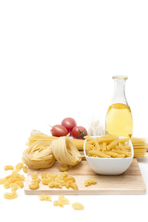 Italian pasta, macaroni quills with cherry tomatoes and olive oil in a glass bottle on a wooden board, white backgroundの写真素材