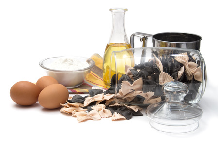 Italian pasta, colorful farfalle with cuttlefish ink and salmon in a glass container with a lid, olive oil, eggs and flour on white backgroundの写真素材