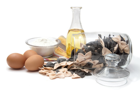 Italian pasta, colorful farfalle with cuttlefish ink and salmon in a glass container with a lid, olive oil, eggs and flour on white backgroundの写真素材