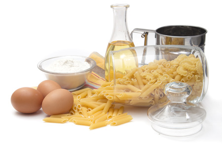 Italian pasta Pennette Rigate in a glass container with a lid, olive oil, eggs and flour on white backgroundの写真素材