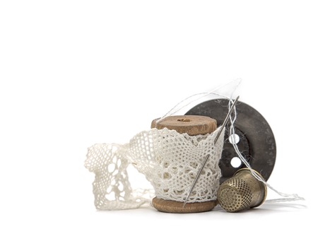 wooden vintage spool for thread wound with white lace for sewing, needle, black wooden button and a metal thimble on white background, retro accessoriesの写真素材