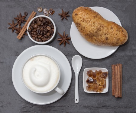 Coffe, a cup of hot latte or cappuccino with bun, top view. Background plate made from natural...
