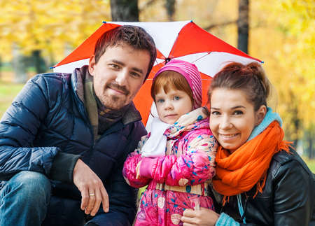 Happy young family under an umbrella in an autumn parkの写真素材