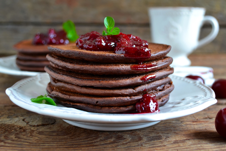 chocolate pancakes with berry jam for breakfast on a wooden backgroundの写真素材