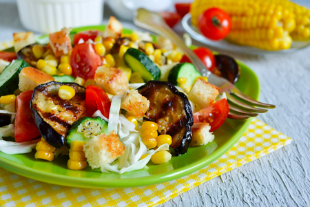 Salad with corn, tomatoes, eggplant and grilled croutons on a concrete backgroundの写真素材