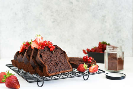 Chocolate muffin with strawberries and currants on a light concrete background. Pieces of cake....