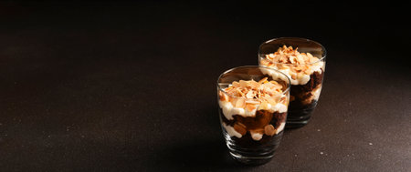 Chocolate cake in a glass with vanilla cream and almonds. A portion of dessert in a glass on a dark...