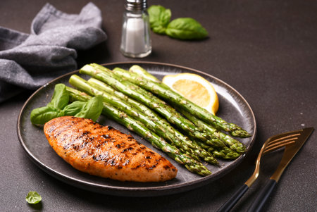 Baked asparagus and grilled chicken fillet in a plate on a dark backgroundの写真素材