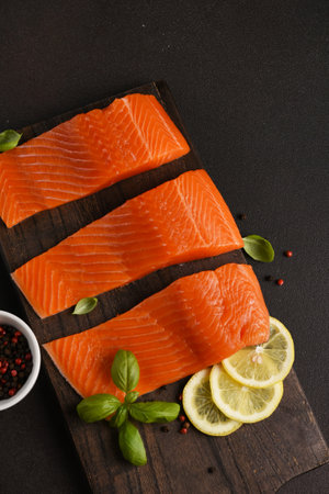 Salmon pieces on a wooden board on a dark background with lemon and spicesの写真素材