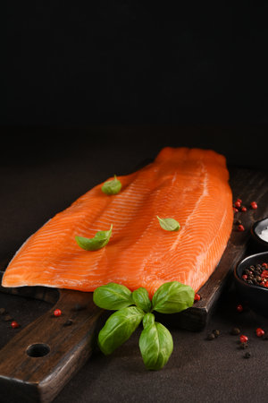 Salmon pieces on a wooden board on a dark background with spicesの写真素材