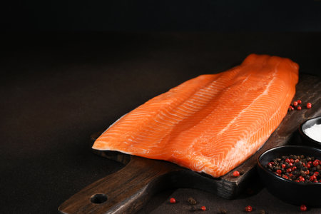 Salmon pieces on a wooden board on a dark background with lemon and spicesの写真素材