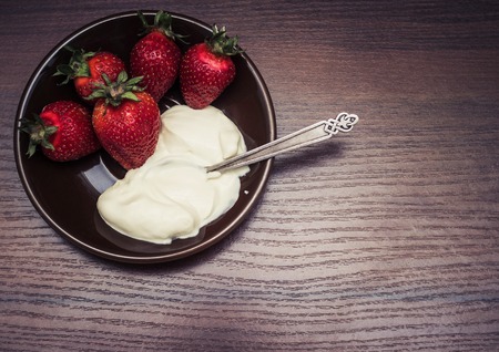 Strawberries with a spoon of cream on a plateの写真素材