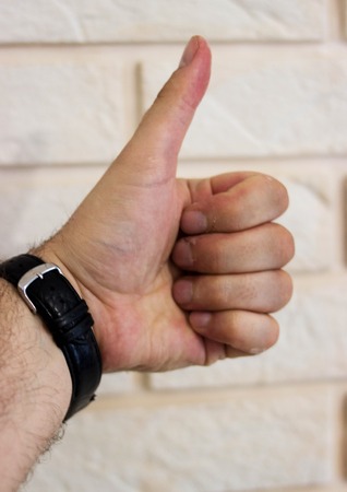Gesture thumbs up, male hand against a white wall backgroundの写真素材
