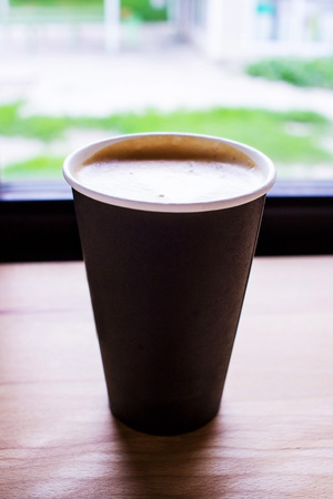 A large glass with fresh coffee lies on the windowsill near the windowの写真素材