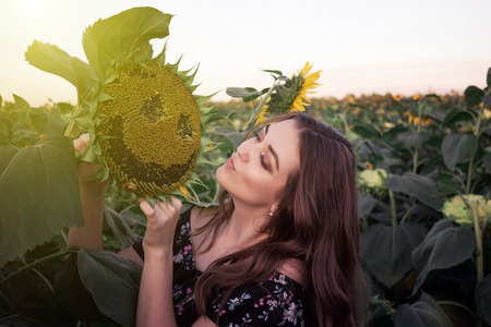 Summer girl. Beautiful cheerful young woman with sunflower enjoying nature and laughing on summer sun flower field. Sunflare, sunbeams, glow sun. Backlightの写真素材