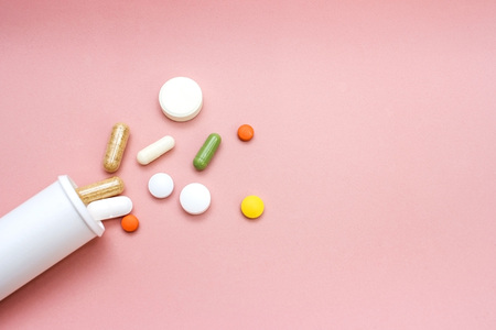 Different pills drugs or tablets spilling out of a white plastic medicine bottle aspirin or paracetamol antibioticsの写真素材