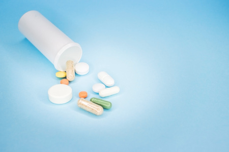 Multi-colored tablets and capsules, white bottle for tablets, pharmaceutical medicine pills on blue...
