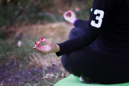 Beautiful blonde caucasian girl in green swimsuit doing asana balancing on her shoulders with twisted legs in the air on a sunny summer day in park. Yoga concept. Healthy lifestyle concept.の写真素材